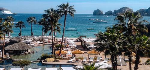 Picture of a beautiful beach resort in Jaco Beach.  The picture shows a marina, palm trees, a harbor, blue water and rocks rising from the water.