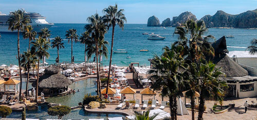 Picture of a beautiful beach and harbor in La Marina Resort in Jaco.  The picture shows, palm trees, boats in the harbor, blue skies and blue water.