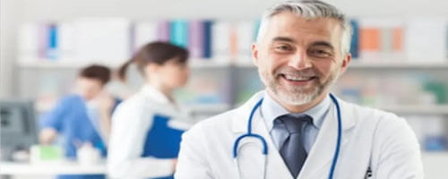 Picture of a plastic surgeon representing the doctors at Top Plastic Surgeons in San José, Costa Rica.  The picture shows a doctor in a white coat with a stethoscope around his neck and arms crossed, looking directly at the camera and smiling.